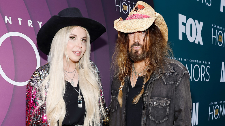 Billy Ray Cyrus and Firerose stand together on red carpet