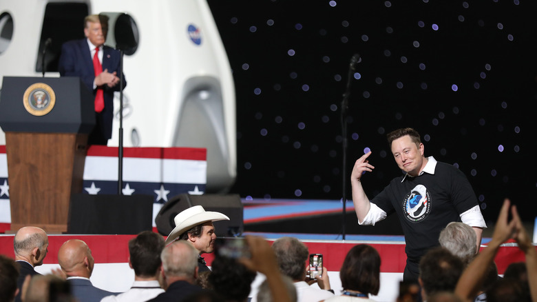 Donald Trump clapping onstage, Elon Musk standing in crowd