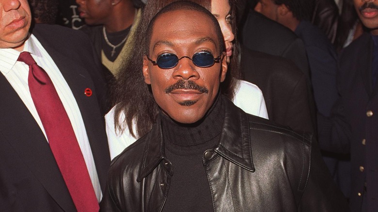 Eddie Murphy wearing blue-tinted glasses, black turtleneck, and black leather jacket