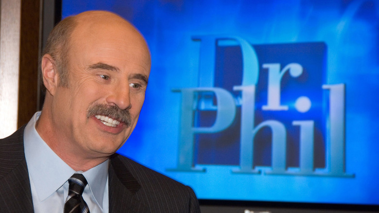 Dr. Phil smiles in front of a Dr. Phil monitor screen