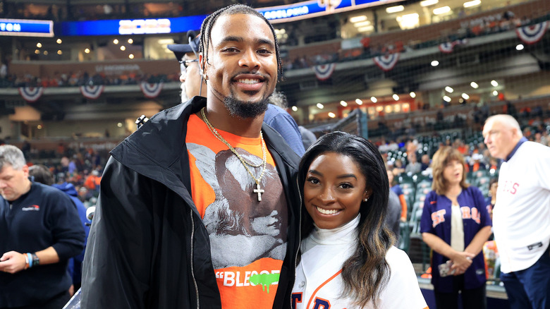 Jonathan Owens wearing a black jacket and orange t-shirt with Simone Biles wearing a white turtleneck and baseball jersey