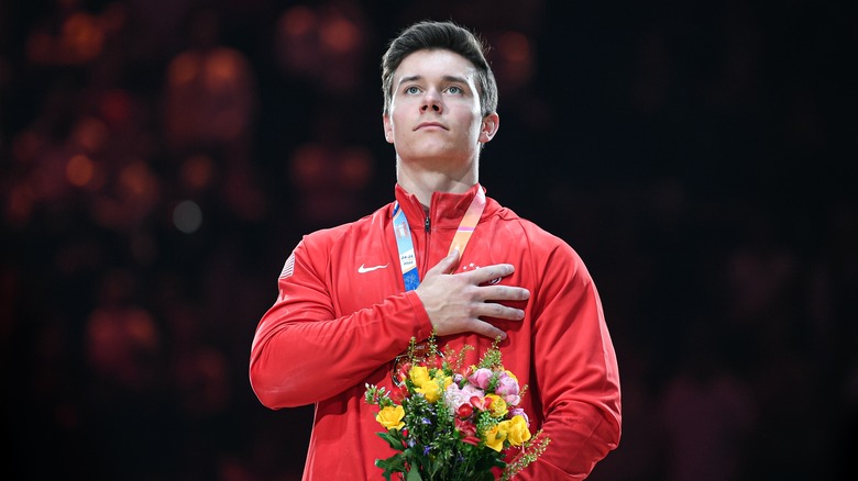 Brody Malone wearing a red jacket with his hand over his heart while holding flowers